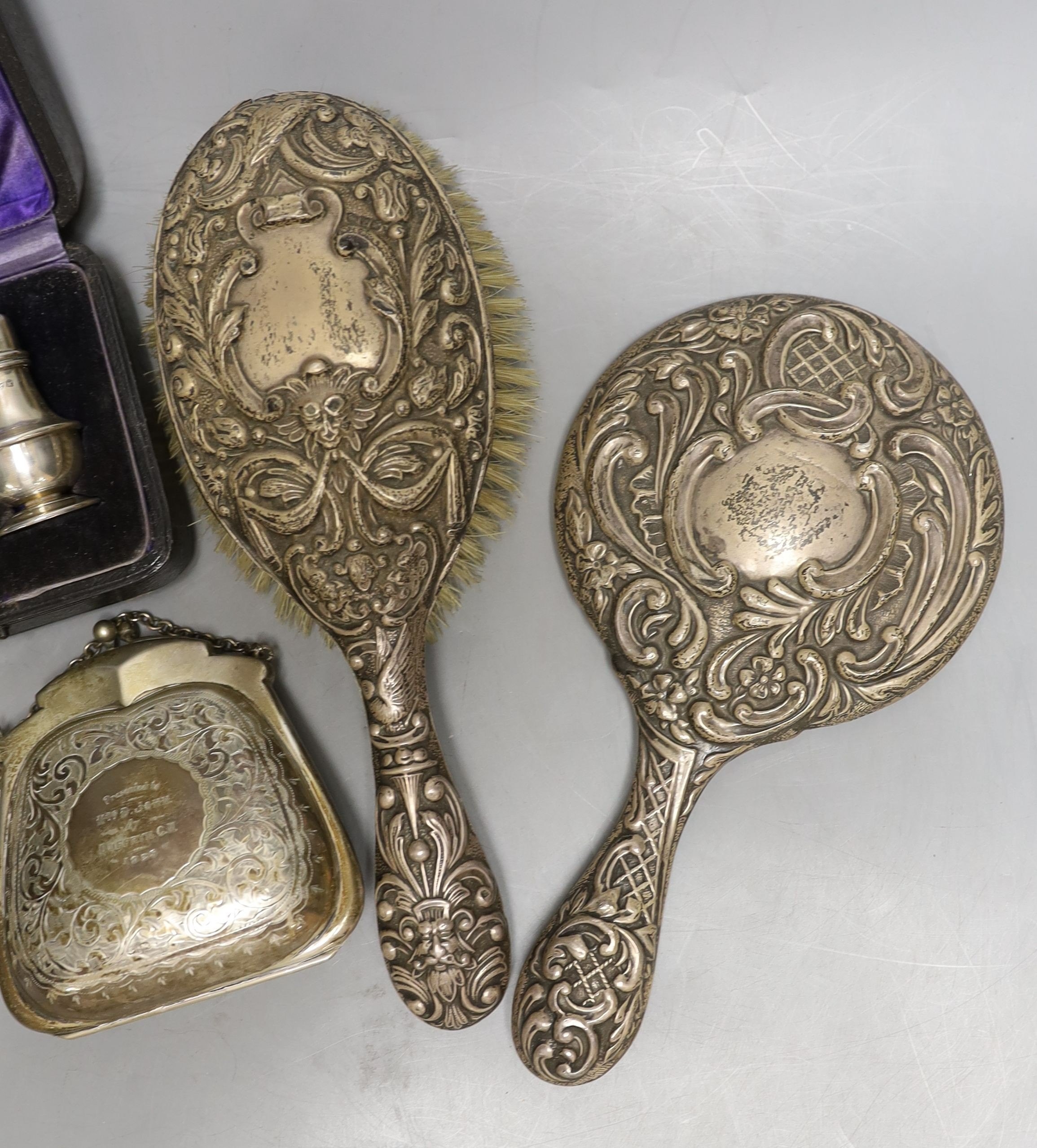 A cased pair of George V silver condiments, an engraved silver purse, silver mounted mirror and brush an a child's silver rattle.